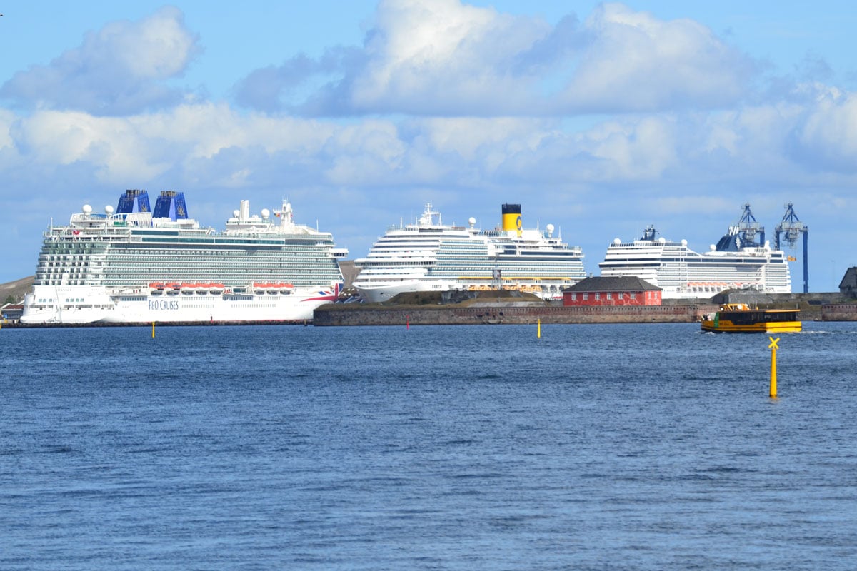 Aus der Ferne sind drei große Kreuzfahrtschiffe zu sehen, die hintereinander im Industriehafen von Kopenhagen festgemacht haben.