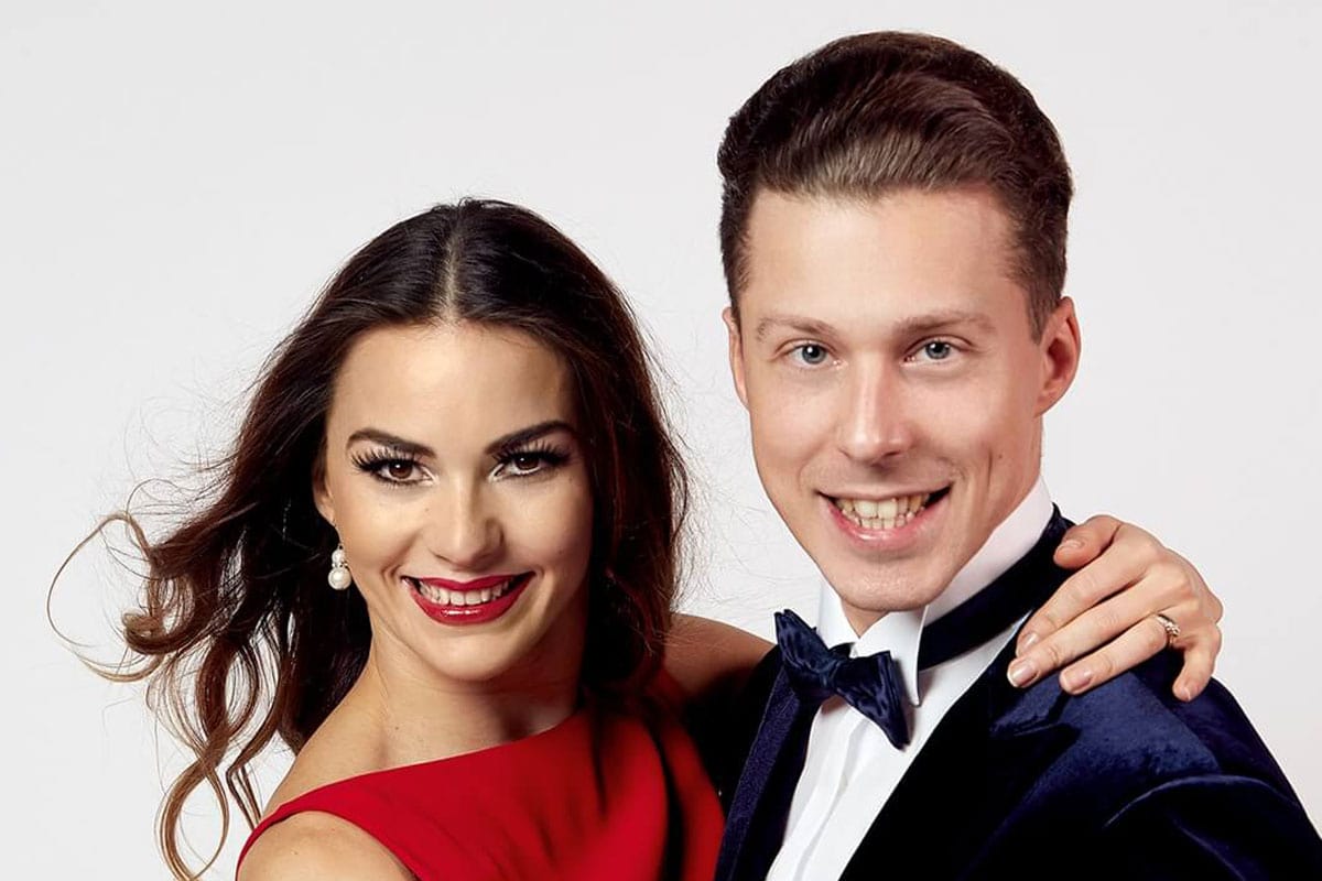 Die Tanzprofis Renata und Valentin Lusin, bekannt aus der TV-Show Let´s Dance, stehen in Tanzkleidung zusammen und blicken in die Kamera. Sie trägt ein rotes Kleid, er einen Smoking mit Fliege.