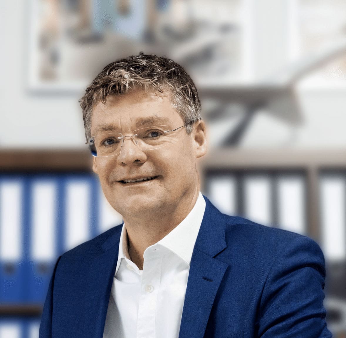 Ein Mann im blauen Anzug sitzt in einem modernen Büro mit weißen und blauen Aktenordnern im Hintergrund, auf einem Regal steht ein Modellflugzeug. Das Bild vermittelt einen professionellen Geschäftskontext, passend für die Themen Luftfahrt, Airline-Management und Unternehmensberatung.