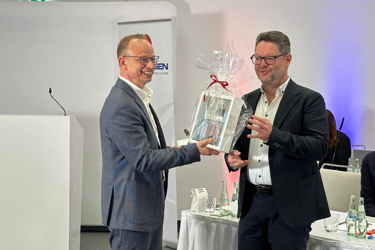 Zwei Männer stehen sich gegenüber. Der eine übergibt dem anderen ein Geschenk