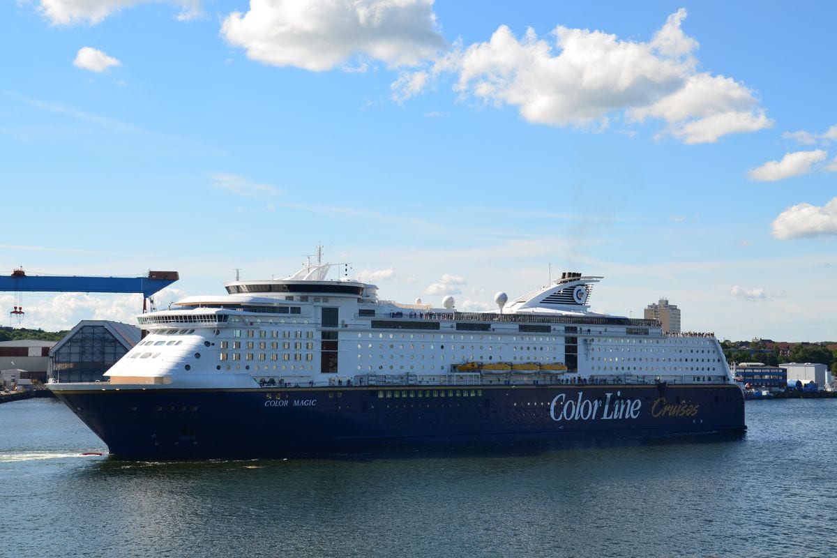 Die Fähre „Color Magic“ von Color Line liegt bei sonnigem Wetter im Hafen; das große weiß-blaue Schiff ist seitlich auf ruhigem Wasser zu sehen, darüber ein blauer Himmel mit einzelnen Wolken.
