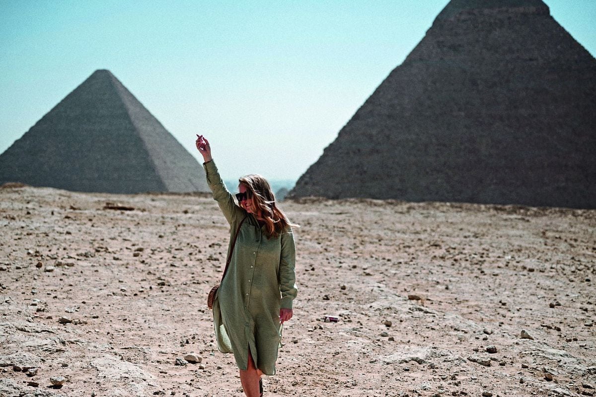 Christin Reiber, Senior Marketing Managerin beim Ägypten-Reisespezialisten Ecco Reisen, steht in einem grünen Kleid und mit Sonnenbrille in der Wüste vor den Pyramiden von Gizeh und streckt lächelnd einen Arm in die Höhe.