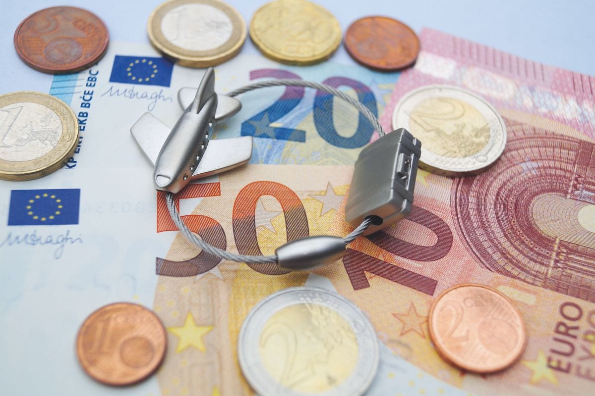 Euro-Banknoten und Münzen mit kleinem Flugzeug-Anhänger und Kabelschloss als Symbol für Kosten und Gebühren bei Flugreisen.