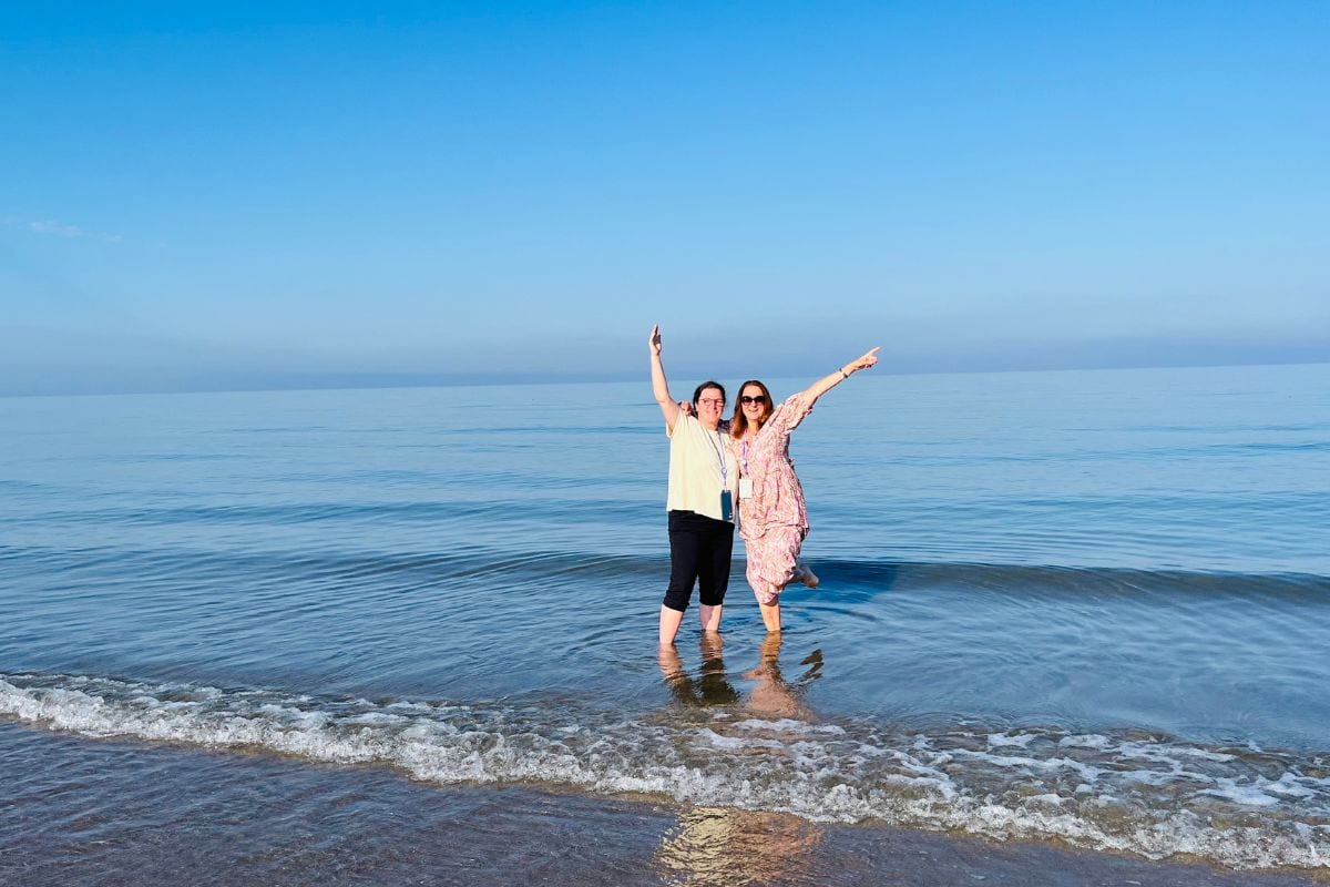 Zwei Frauen stehen im Meer und rechen die Arme in die Höhe