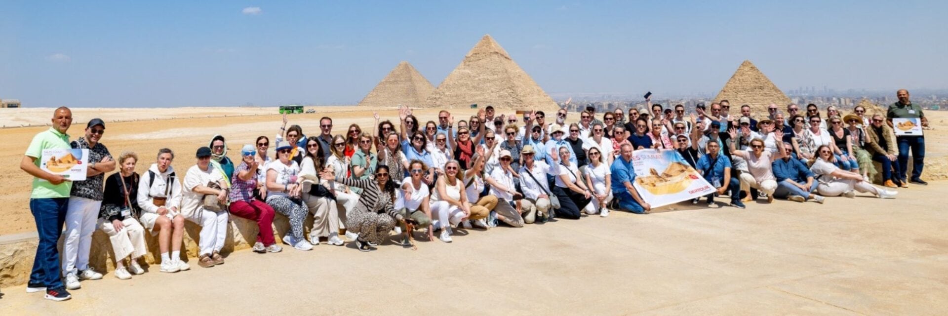 Große Gruppe von Teilnehmenden des DERTOUR Group Sales Summit vor den Pyramiden von Gizeh in Ägypten, viele winken in die Kamera.