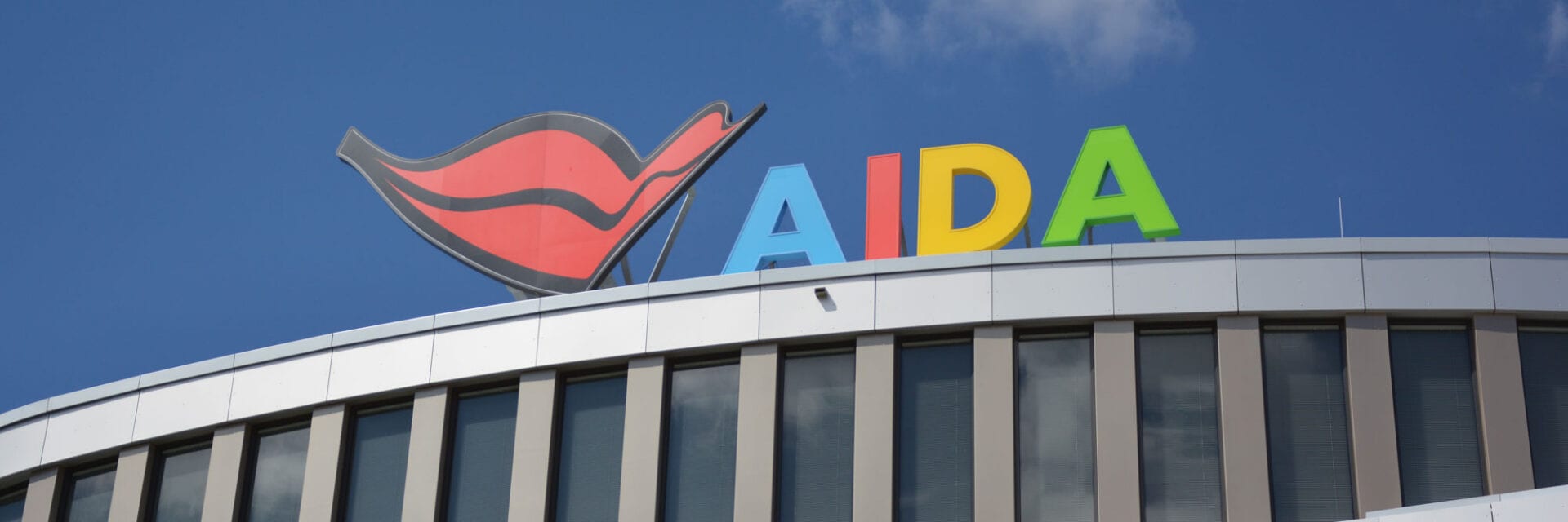 Auf der Zentrale des Kreuzfahrtanbieters Aida ist der logohafte bunte Namensschriftzug vor hellblauem Himmel zu sehen.