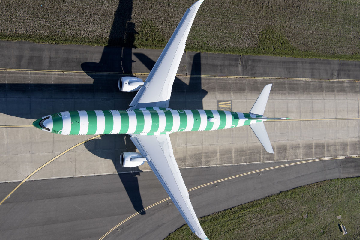 Aus der Vogelperspektive ist ein Condor Airbus A330 Neo mit markanter grün-weißer Streifenlackierung auf dem Rollfeld eines Flughafens zu sehen, die Flügel und Triebwerke sind vollständig sichtbar. Das moderne Langstreckenflugzeug steht auf einer Betonfläche, umgeben von Gras und Asphalt.