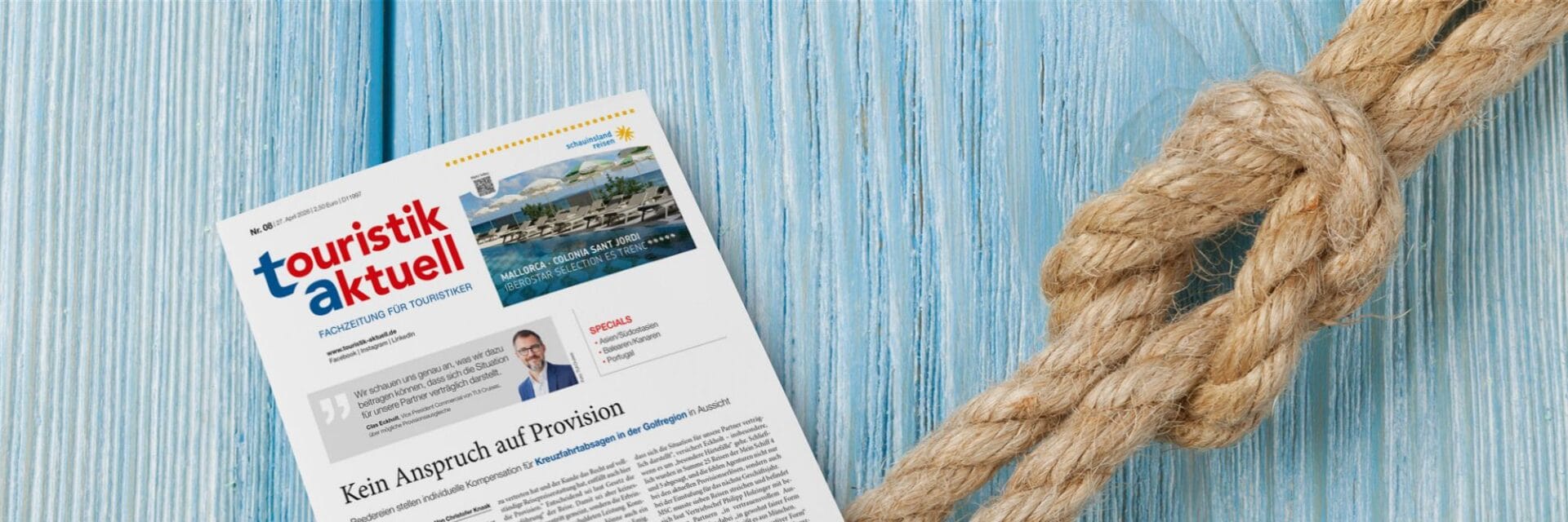 Magazin „touristik aktuell“ auf blauem Holzhintergrund neben einem Seil; Titelthema zu Provisionsfragen bei Kreuzfahrtabsagen sichtbar.