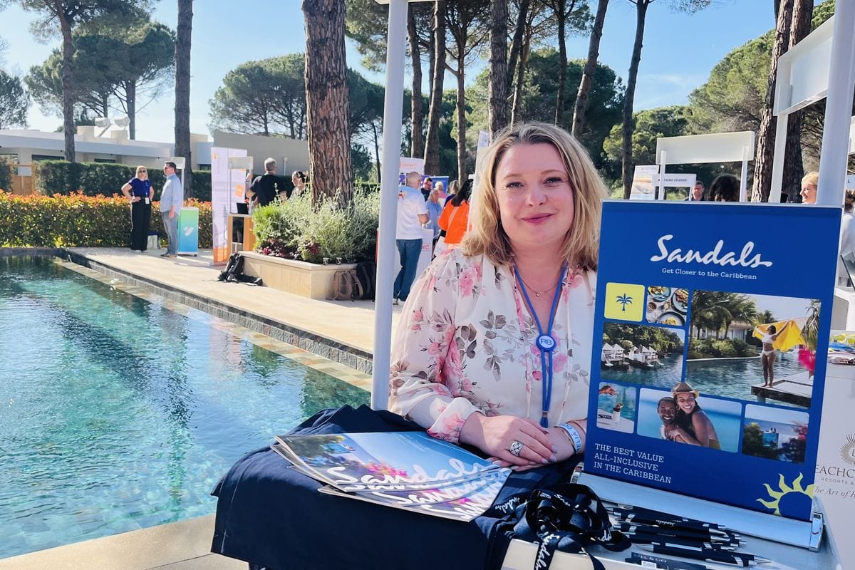 Eine Frau steht an einem Stand und präsentiert die Marke Sandals. Im HIntergrund sind Menschen und ein Pool zu sehen