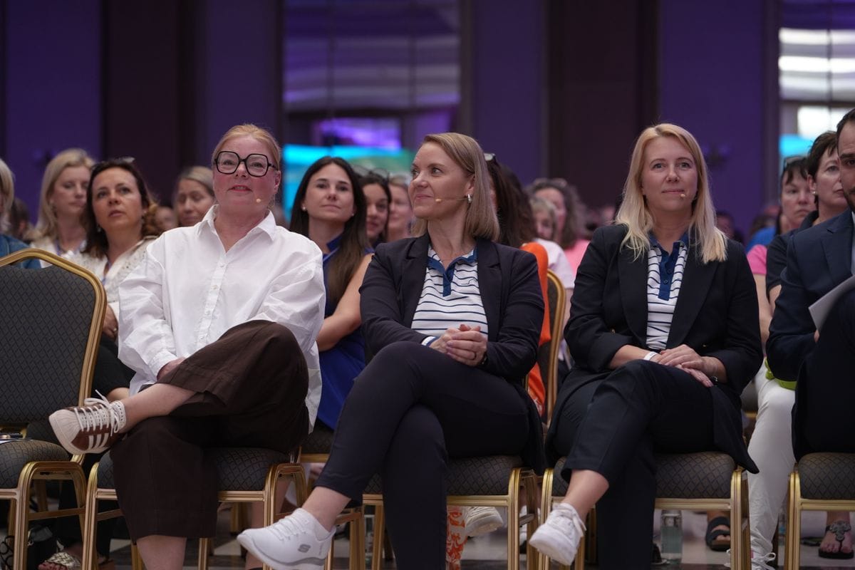 Drei Frauen sitzen in der ersten Reise eines saals und haben Mikrofone.