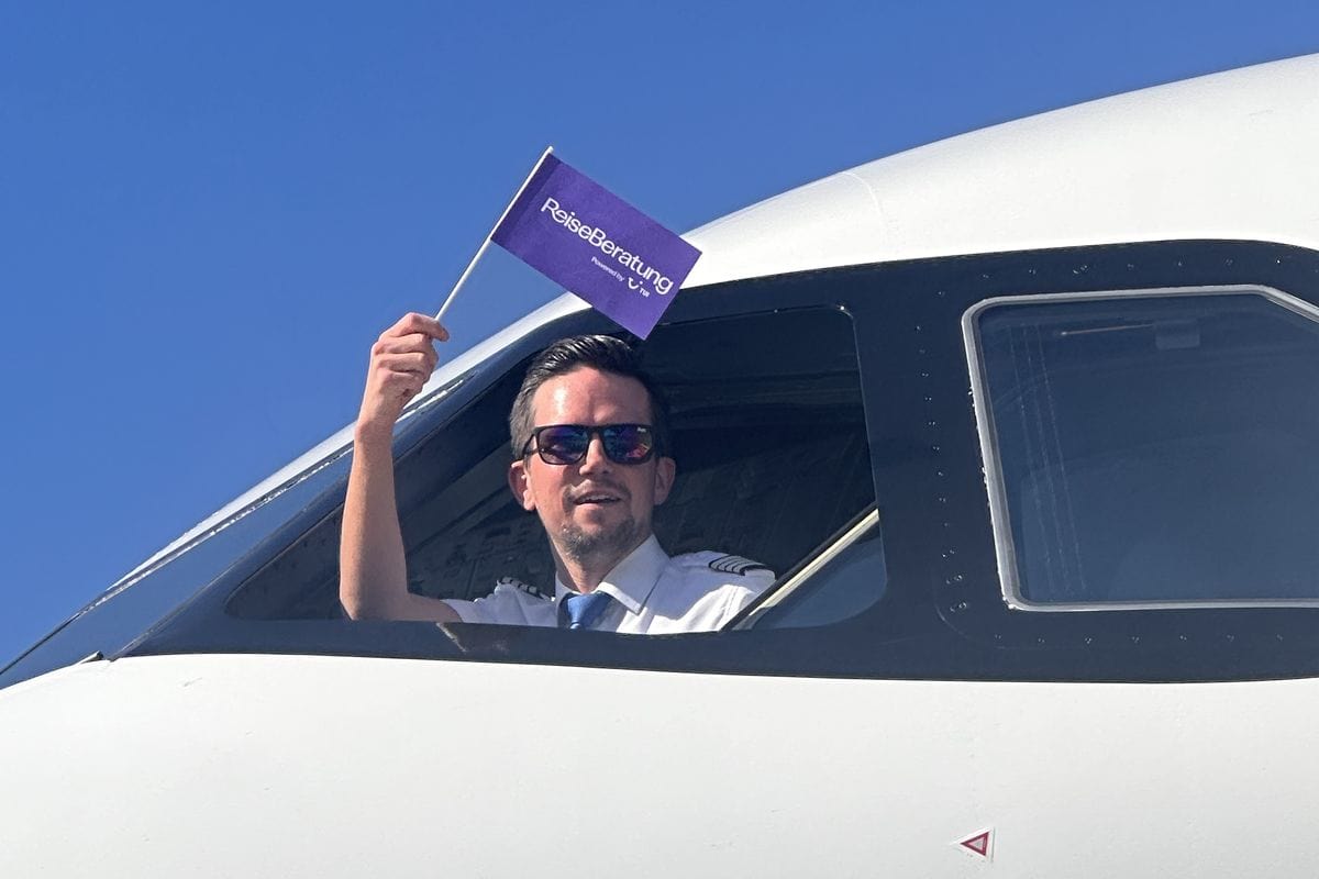 Ein Pilot blickt aus dem Fenster eines Flugzeuges und winkt mit einem Fähnchen auf dem Reiseberatung steht