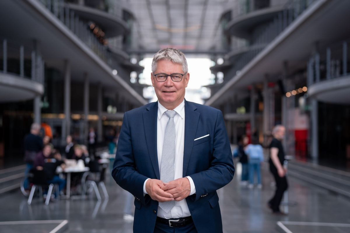 DRV-Präsident Albin Loidl steht in einem modernen, lichtdurchfluteten Gebäude mit Glasarchitektur. Im Hintergrund sind Menschen und Tische sichtbar.