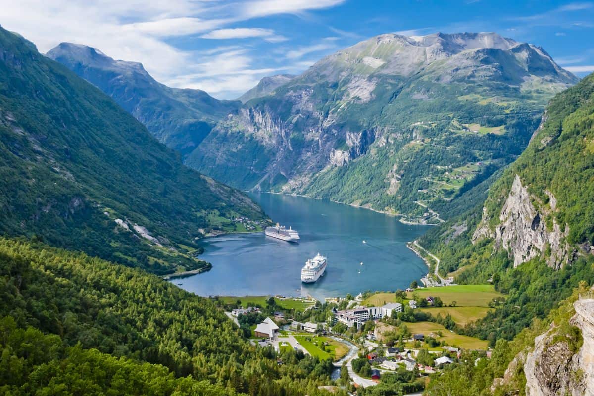 Panoramablick auf einen Fjord mit zwei Kreuzfahrtschiffen, umgeben von hohen Bergen und üppiger Vegetation in Norwegen.