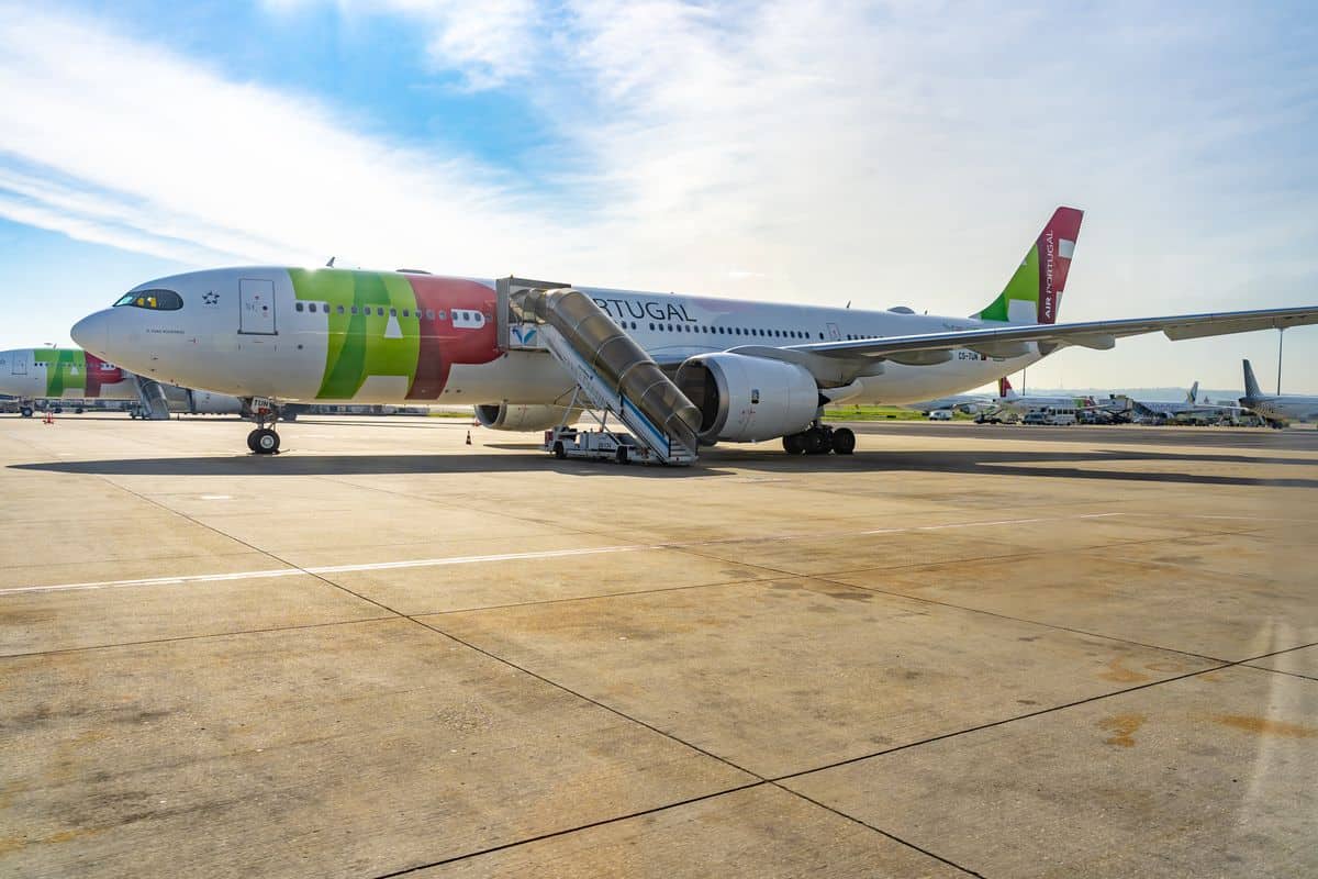 Ein TAP Portugal Flugzeug steht am Flughafen mit einer Treppe, um Passagiere ein- und aussteigen zu lassen. Der Himmel ist klar und blau.