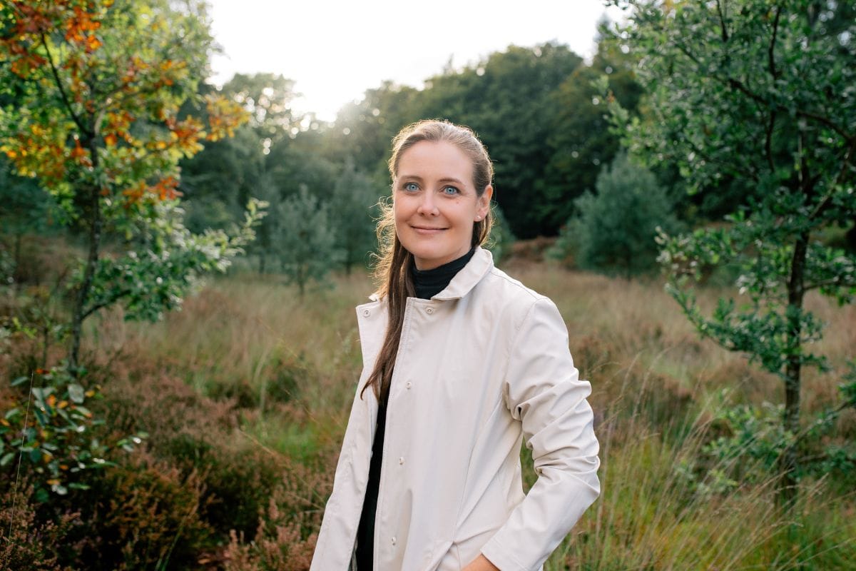 Porträt von Polarsteps-CEO Clare Jones in einer naturnahen Landschaft mit Bäumen und Wiese im Hintergrund.