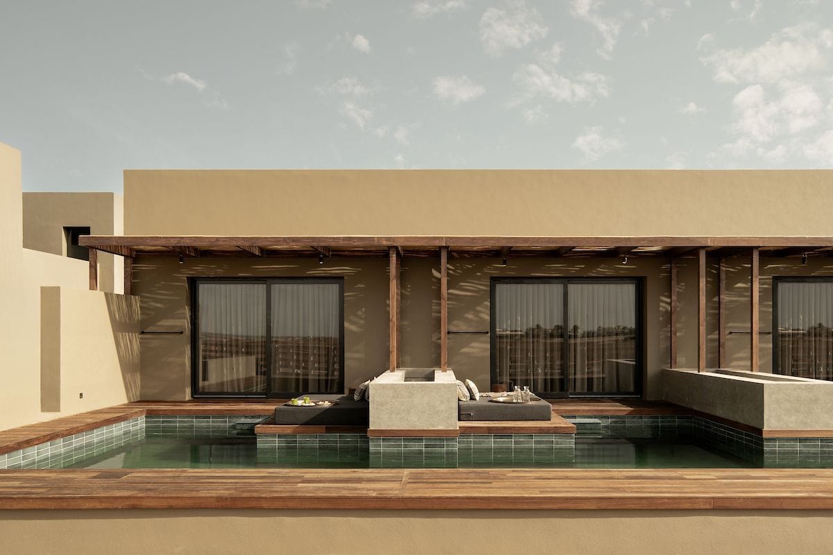 Moderne Architektur eines Hotels mit Holzveranda und Swim-up-Pool, man sieht die minimalistische Gestaltung und die sanften Farben unter einem bewölkten Himmel.