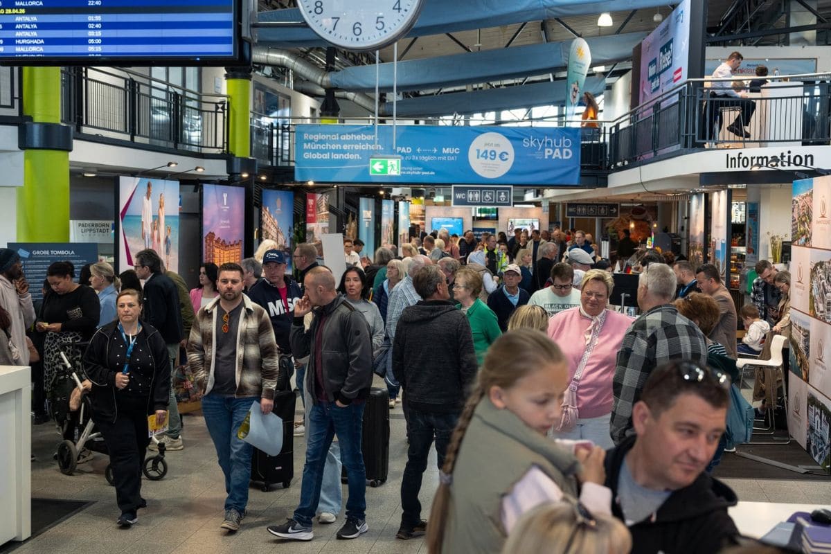 Gut besuchte Reisemesse im Terminal des Flughafens Paderborn: Zahlreiche Besucher bewegen sich zwischen Messeständen internationaler Reiseanbieter, während Anzeigetafeln und Beschilderungen über ihnen hängen.