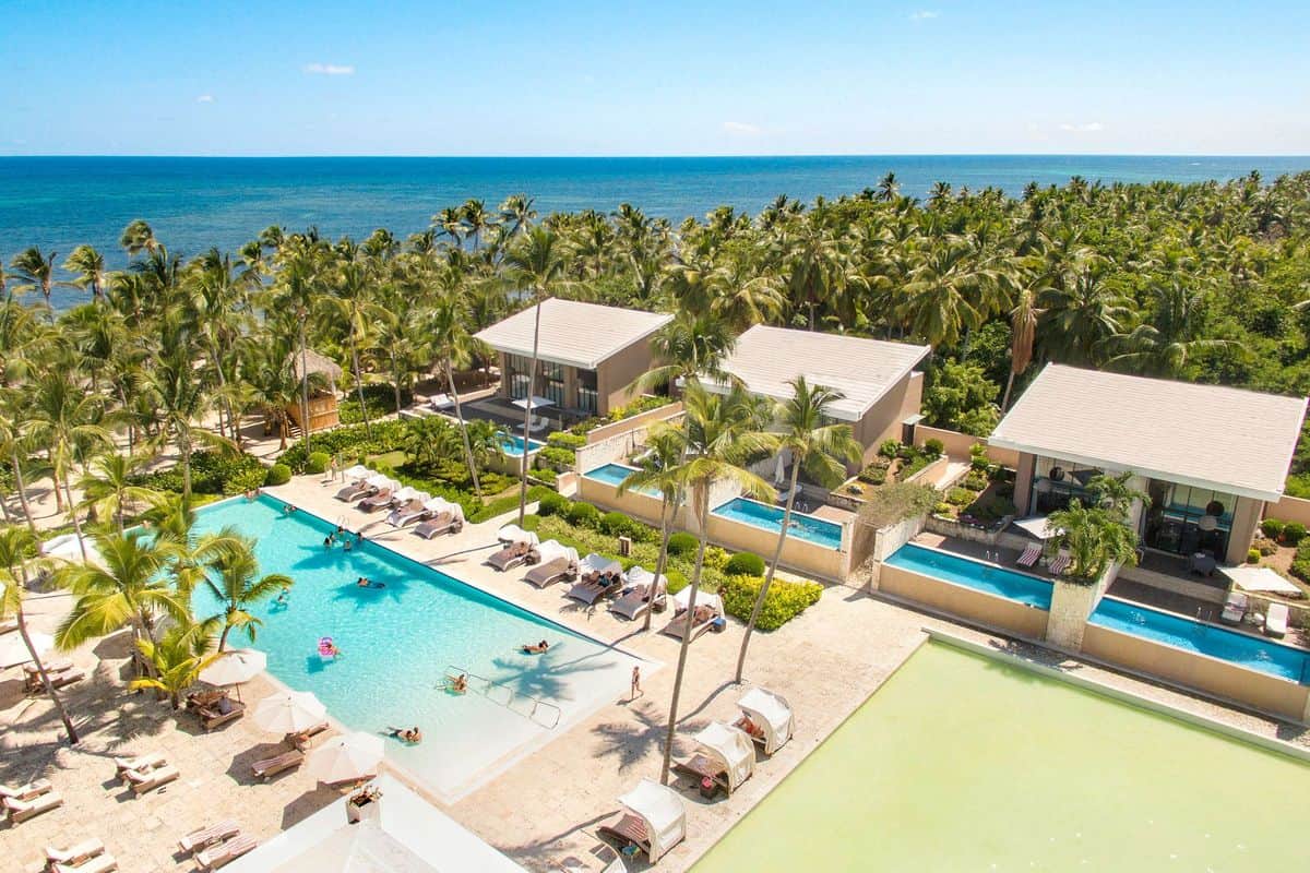 Luftaufnahme eines Resorts mit mehreren Schwimmbädern, Palmen und Blick auf das Meer unter klarem Himmel.