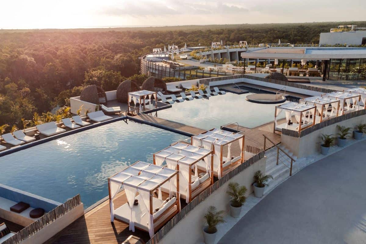 Luxuriöser Infinity-Pool mit Liegen und Cabanas, umgeben von üppiger Vegetation und modernem Architekturdesign, bei Sonnenuntergang.