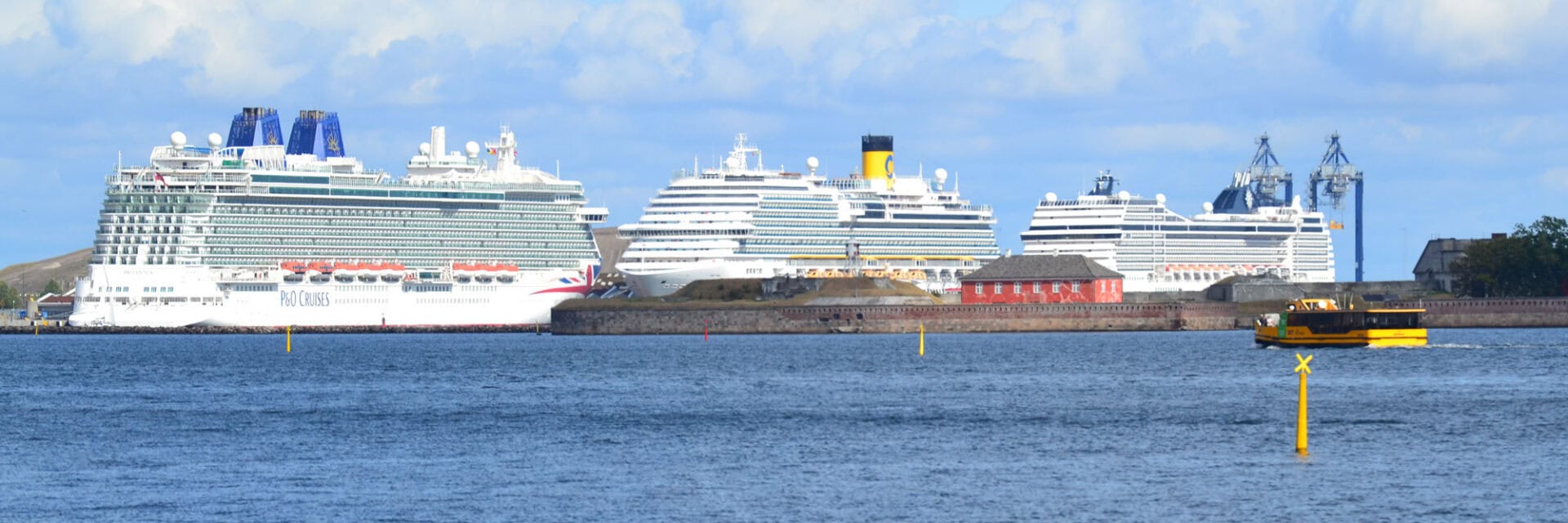 Mehrere Kreuzfahrtschiffe liegen im Hafen, umgeben von Wasser und einem klaren Himmel mit wenigen Wolken.