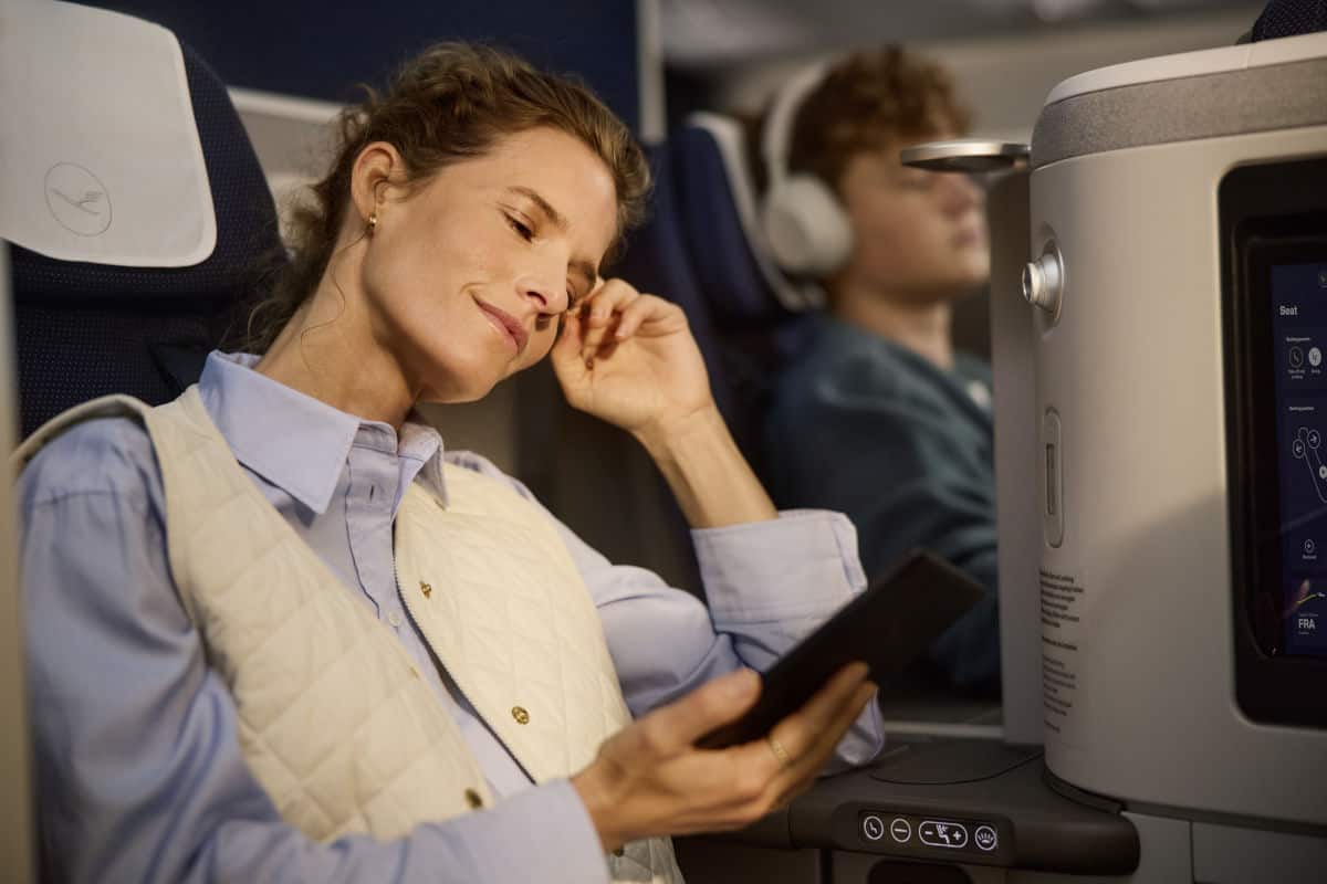 Eine Passagierin in der Lufthansa Allegris Business Class entspannt sich mit einem Smartphone in der Hand, während ein Mitreisender im Hintergrund sitzt.