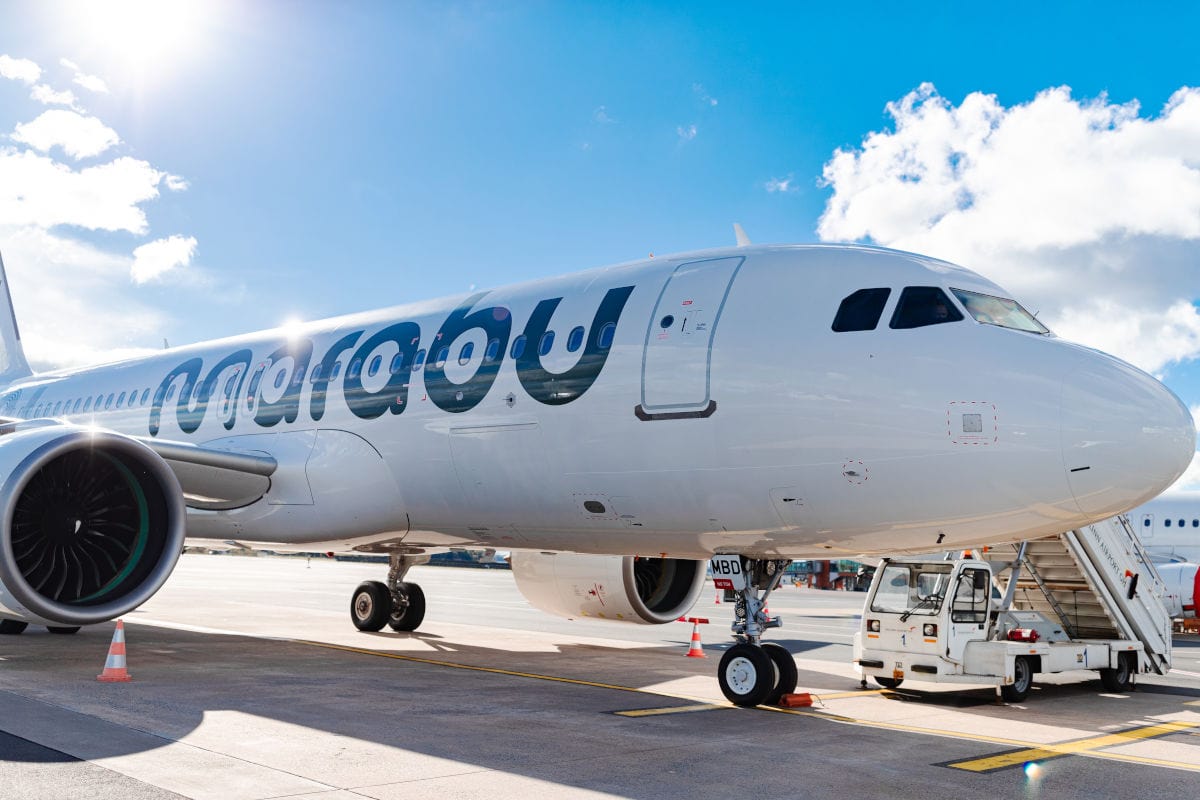 Das Bild zeigt ein modernes Flugzeug von Marabu Airlines am Boden bei strahlend blauem Himmel. Im Vordergrund ist ein Triebwerk klar zu erkennen, während das Flugzeug mit geöffneter Tür auf das Boarding wartet.