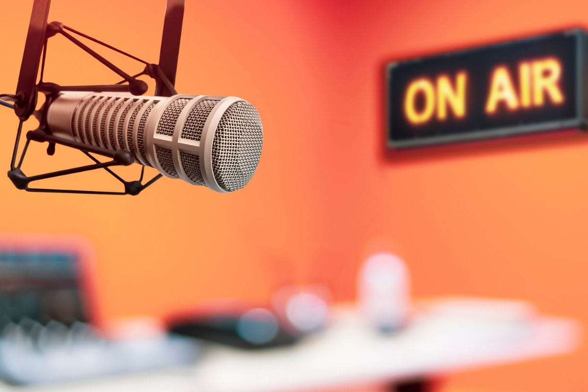 Mikrofon in einem Studio mit einem leuchtenden 'ON AIR'-Schild im Hintergrund, geeignet für Branchenveranstaltungen.