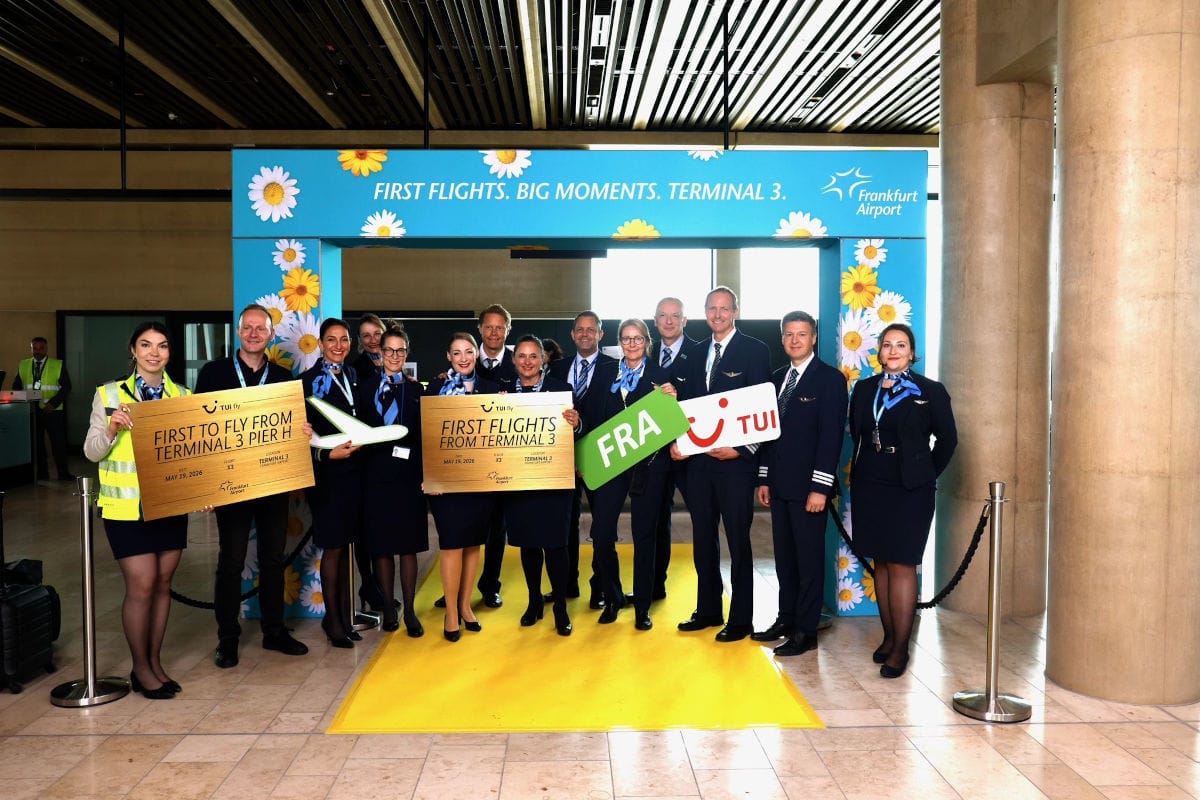 Eine Gruppe von Personen in Uniform steht vor einem bunten Hintergrund mit Blumenmotiven und einem gelben Teppich am Flughafen Frankfurt.