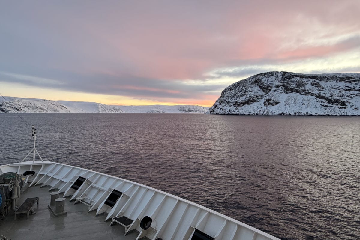 Blick vom Schiff auf die schneebedeckten Berge und das ruhige Wasser in Norwegen während eines Charterflugs mit Vianova.