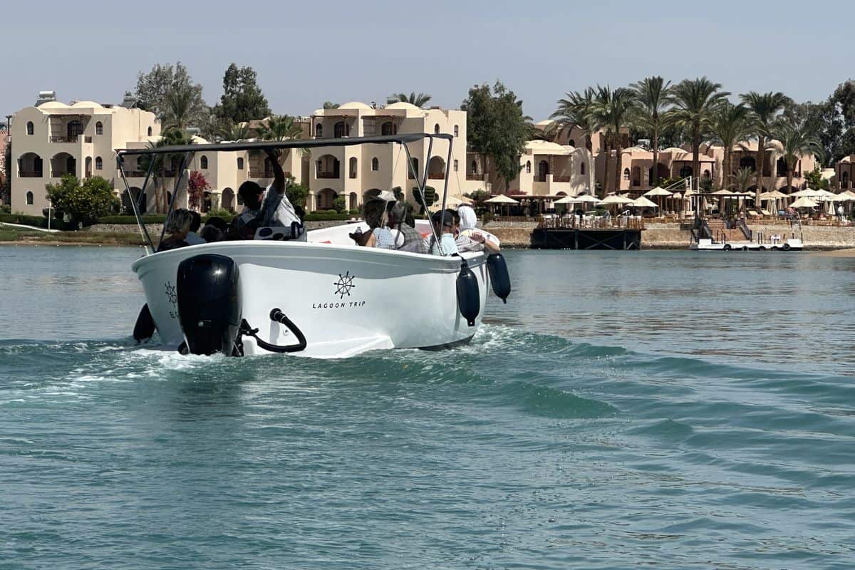 Ein Motorboot fährt durch ruhiges Wasser, im Hintergrund sind elegante Gebäude und Palmen zu sehen, die eine entspannte Atmosphäre schaffen.