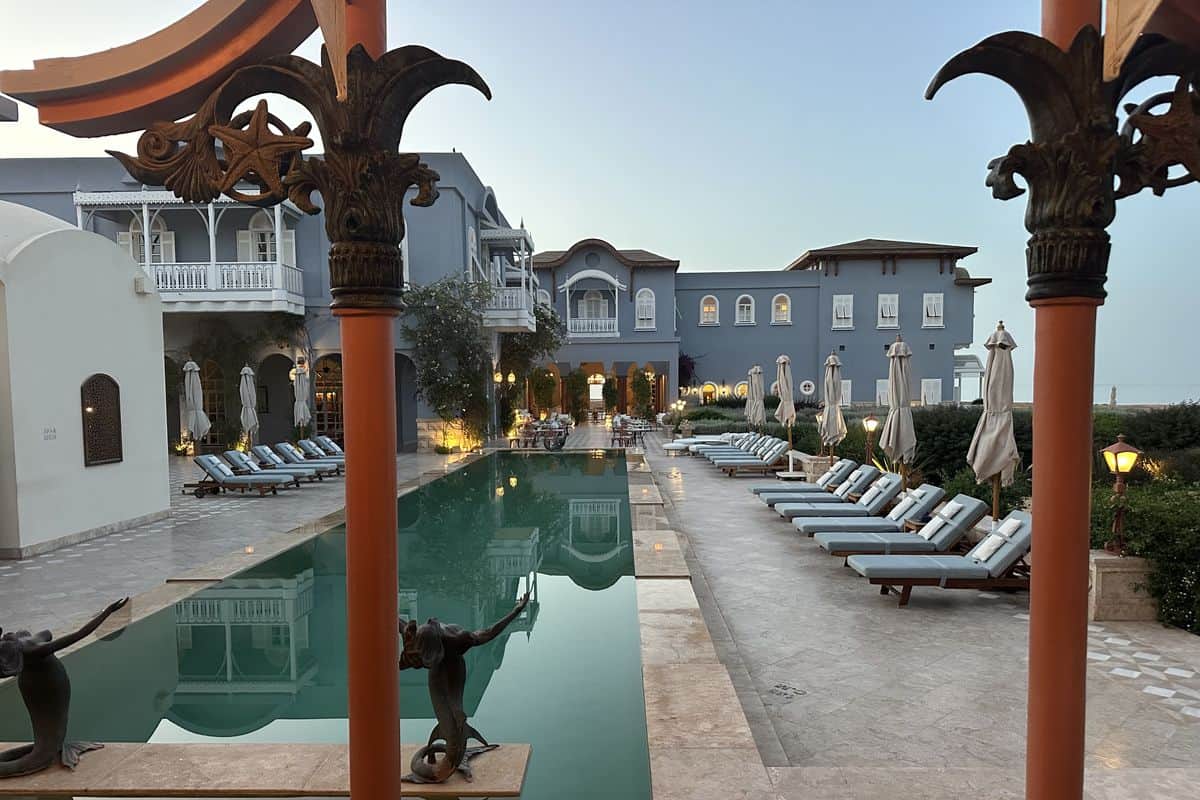 Ein eleganter Außenbereich eines Hotels mit einem Pool, Liegen und Sonnenschirmen, umgeben von gepflegten Pflanzen und einer stilvollen Architektur.