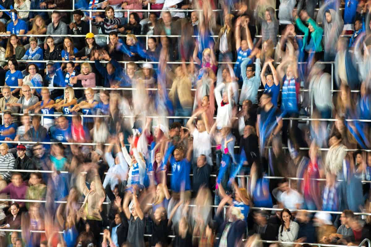 Eine große Menschenmenge in einem Stadion, die sich bewegt und jubelt, mit verschiedenen Kleidungsstilen und Farben, die die Begeisterung widerspiegeln.