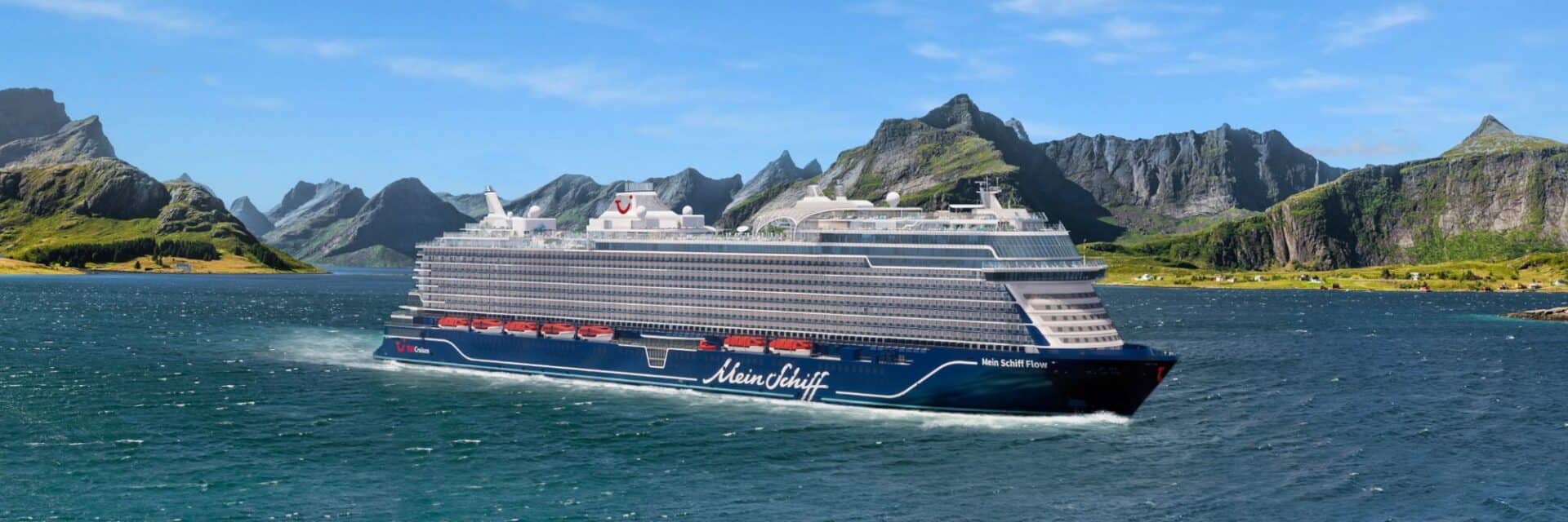 tui-cruises-flow-winterprogramm Ein modernes Kreuzfahrtschiff fährt durch ruhige Gewässer, umgeben von grünen Hügeln und felsigen Bergen unter einem klaren blauen Himmel.
