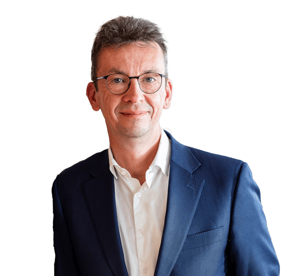 Zitat-Sun-Express-Woelfel_1000x953px Ein Mann mit Brille und kurzem, grauem Haar trägt einen dunkelblauen Anzug und ein weißes Hemd. Er steht vor einem neutralen Hintergrund.