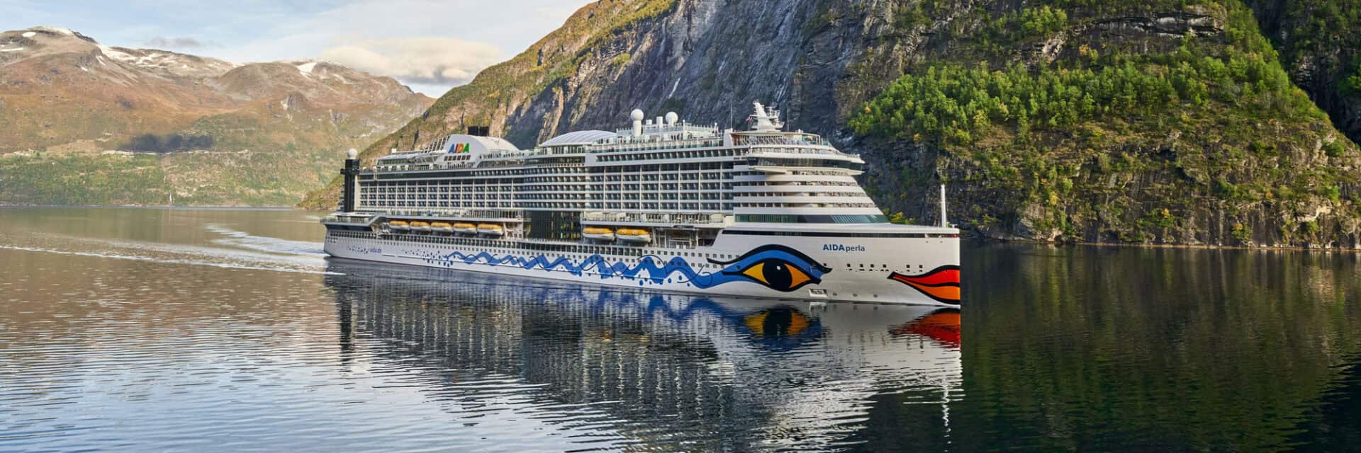 aida-schiff-im-fjord Ein modernes Kreuzfahrtschiff fährt durch einen ruhigen Fjord, umgeben von majestätischen Bergen und üppigem Grün.