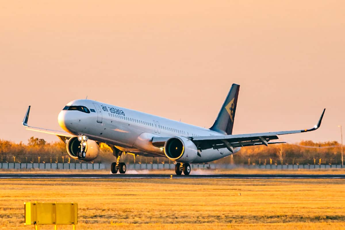 Ein Flugzeug der Airline Air Astana hebt bei Sonnenuntergang von einer Landebahn ab, umgeben von einer goldenen Landschaft.