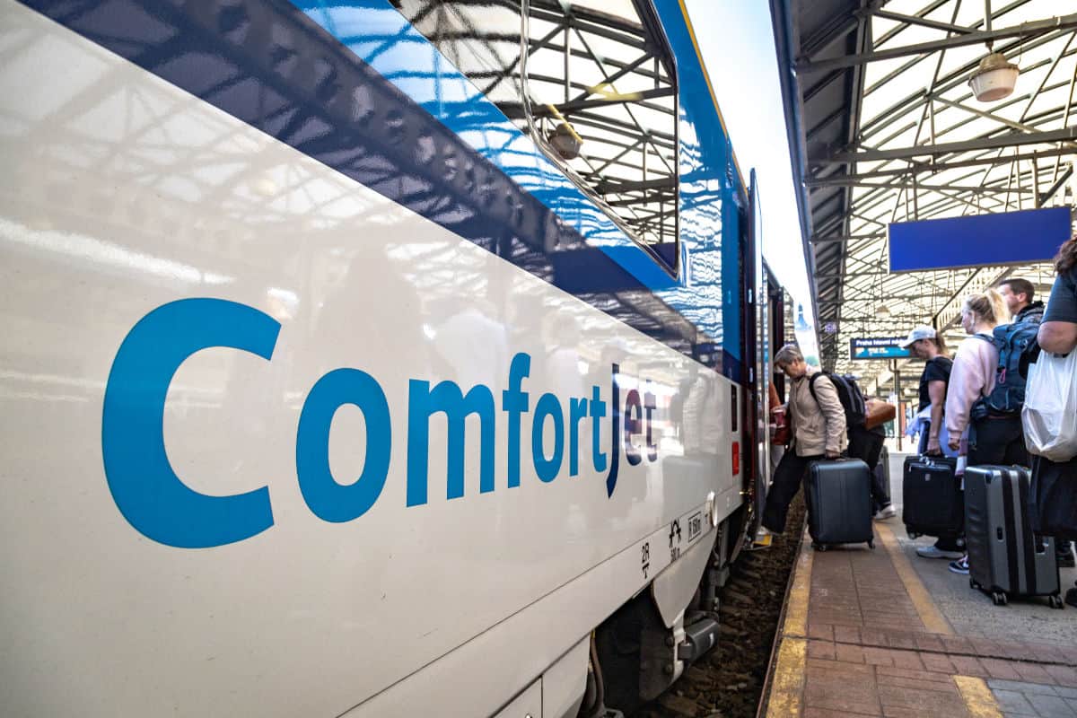 Nahaufnahme eines Zuges mit der Aufschrift 'ComfortJet', während Passagiere mit Gepäck am Bahnsteig einsteigen.