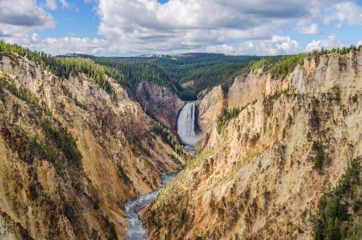 Blick auf den Yellowstone Nationalpark in den USA mit beeindruckenden Klippen und einem Wasserfall, umgeben von üppigen Wäldern.