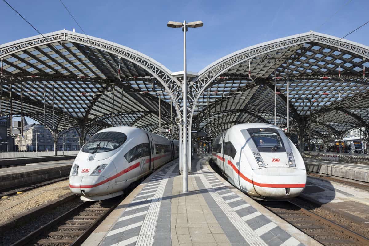 Zwei moderne Hochgeschwindigkeitszüge der Deutschen Bahn stehen an einem Bahnhof unter einem großen, lichtdurchfluteten Dach.