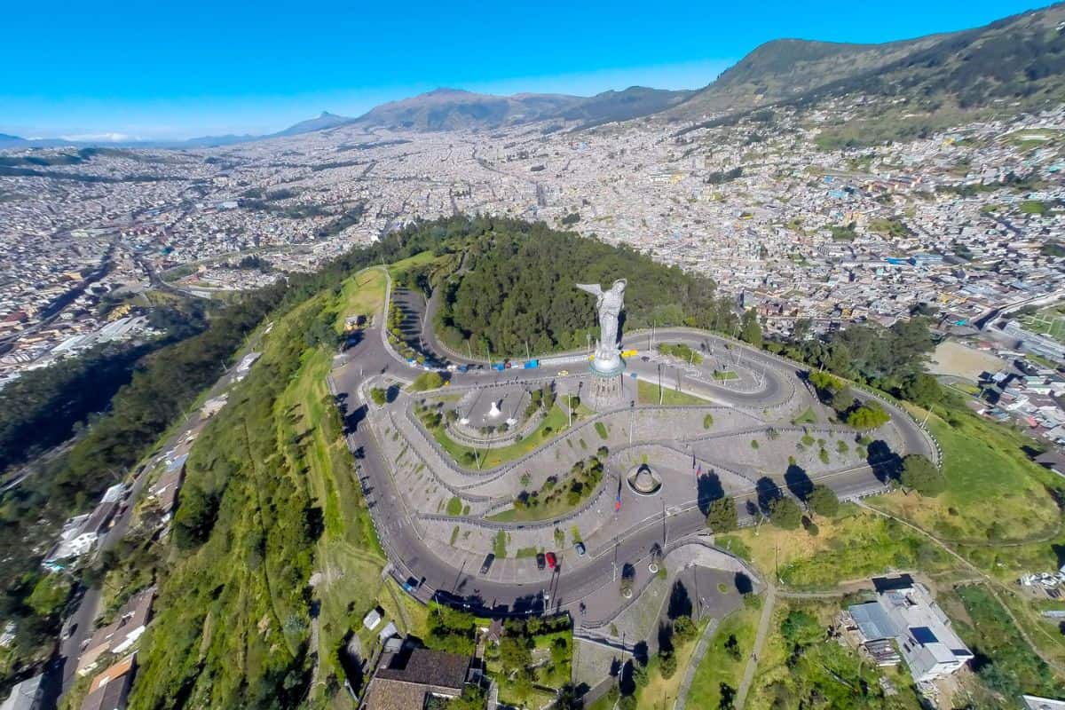 Luftaufnahme einer Stadtlandschaft mit einer Statue auf einem Hügel, umgeben von grünen Bäumen und einer kurvenreichen Straße.