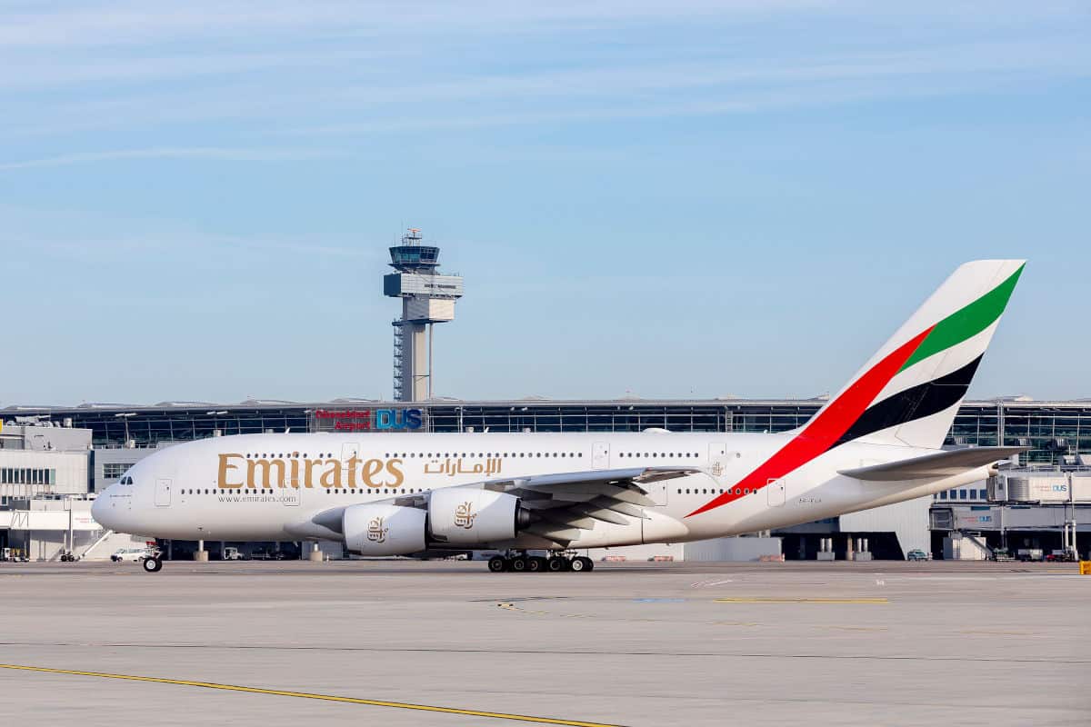 Ein Emirates Airbus A380 steht auf dem Rollfeld eines modernen Flughafens mit einem Kontrollturm im Hintergrund und klar blauem Himmel.
