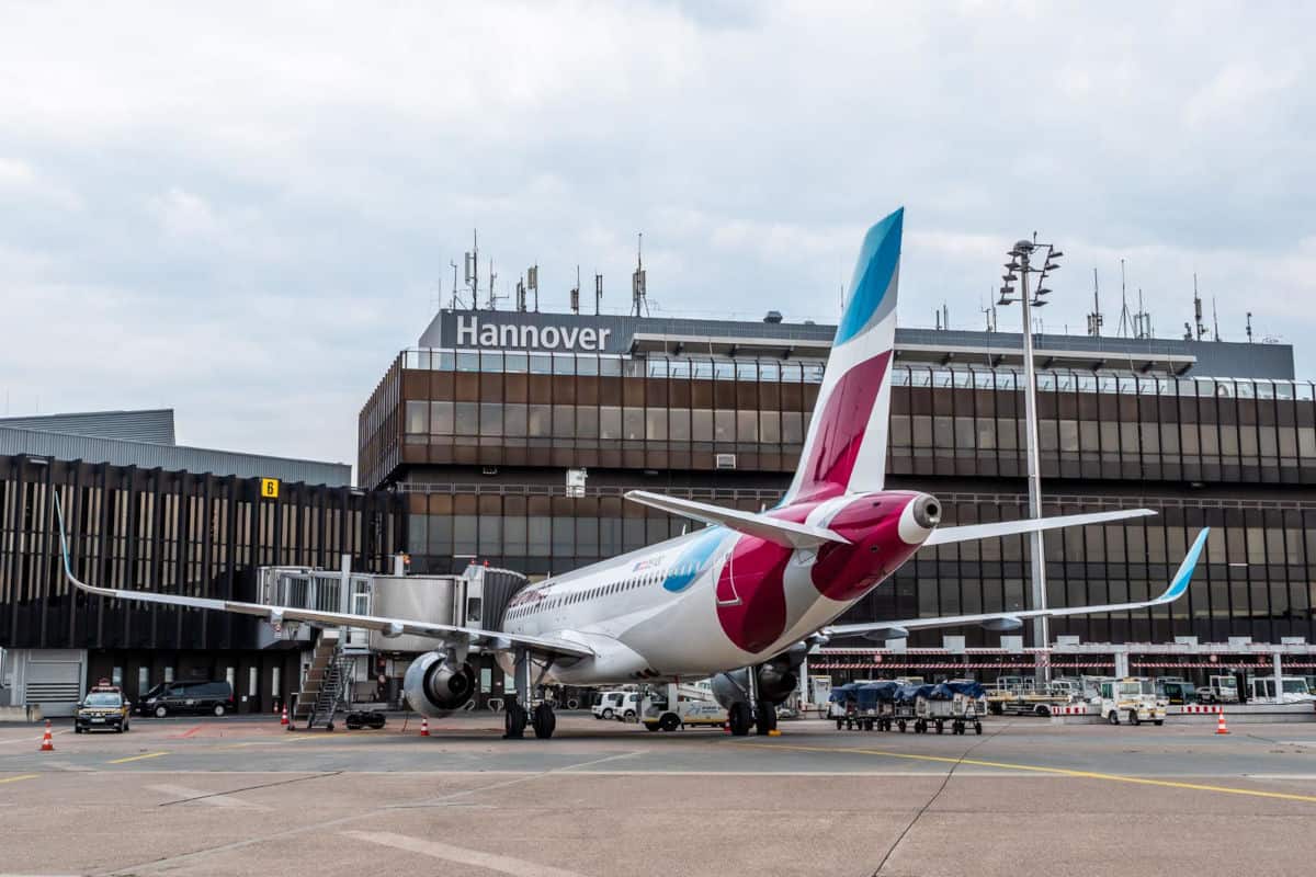 Ein Flugzeug steht am Flughafen Hannover, mit dem Terminal im Hintergrund und einem Wolkenhimmel darüber.