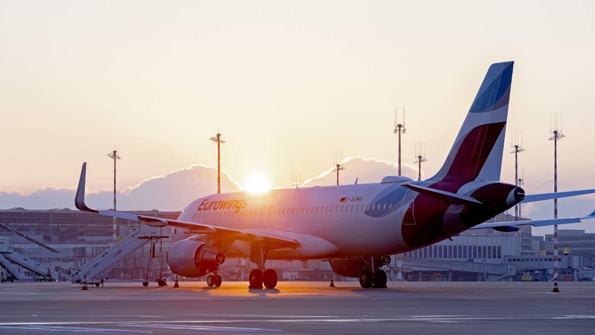 Ein Eurowings-Flugzeug steht auf dem Flughafen Palma de Mallorca, während die Sonne am Horizont aufgeht und die Umgebung in warmes Licht taucht.