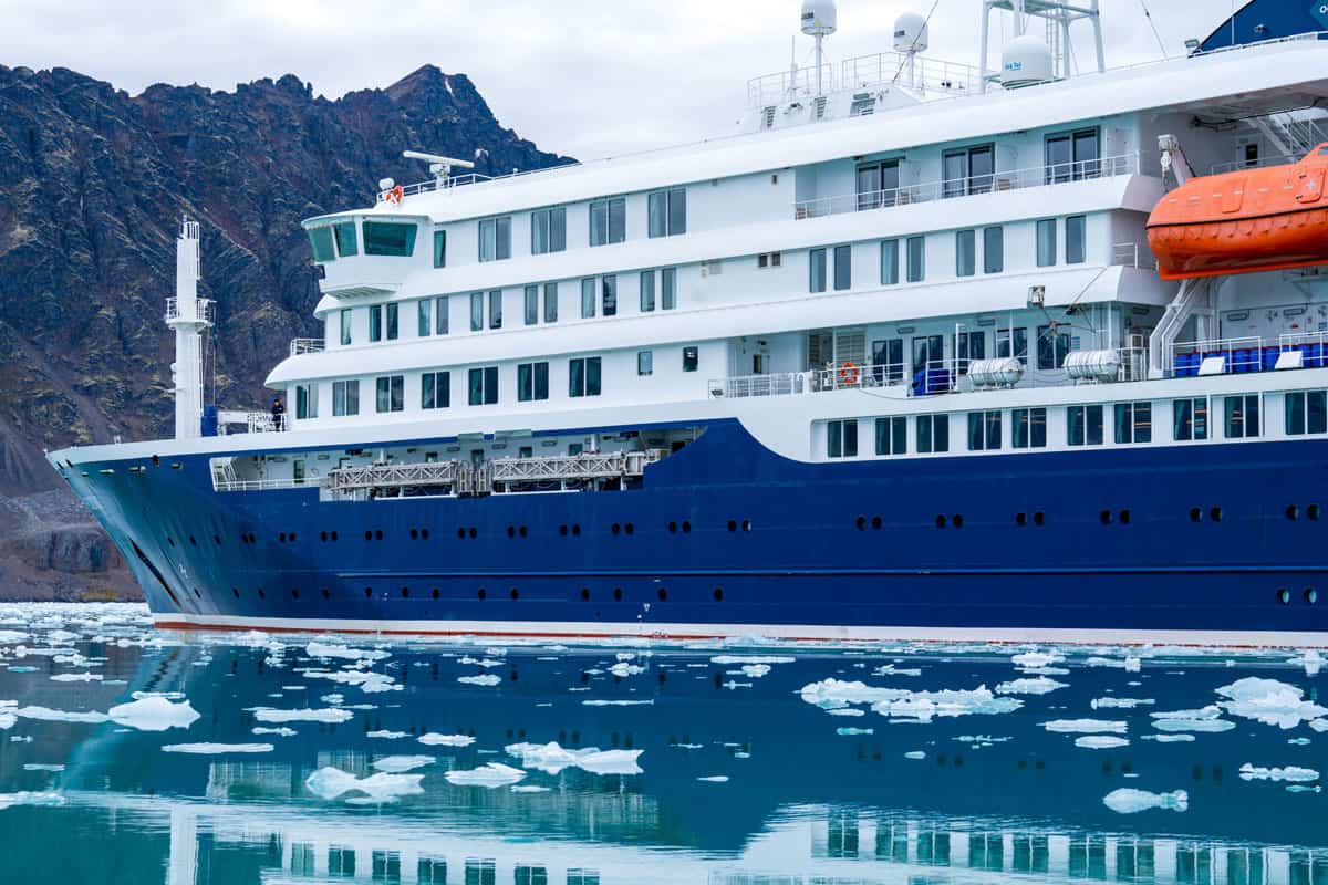 Ein modernes Kreuzfahrtschiff liegt in ruhigem Wasser, umgeben von Eisbergen und majestätischen Bergen im Hintergrund.