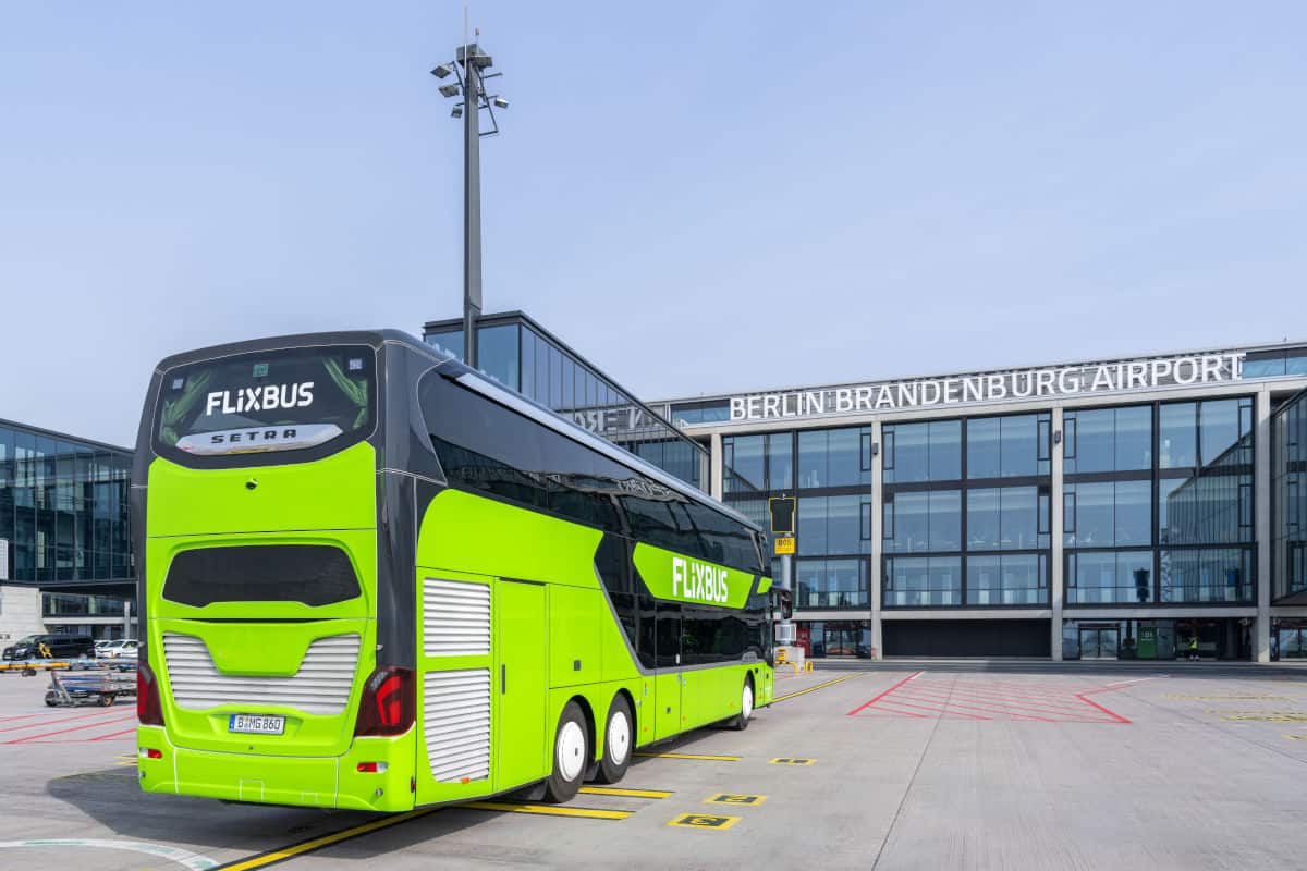 Ein grüner Flixbus der Marke Setra steht vor dem Flughafen Berlin-Brandenburg. Die moderne Architektur des Terminals ist im Hintergrund sichtbar.