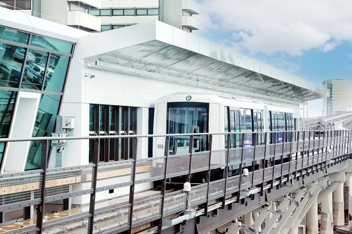Die Sky-Line-Bahn am Flughafen Frankfurt, die an einem modernen Terminalgebäude entlangfährt, umgeben von Glas und Stahl.