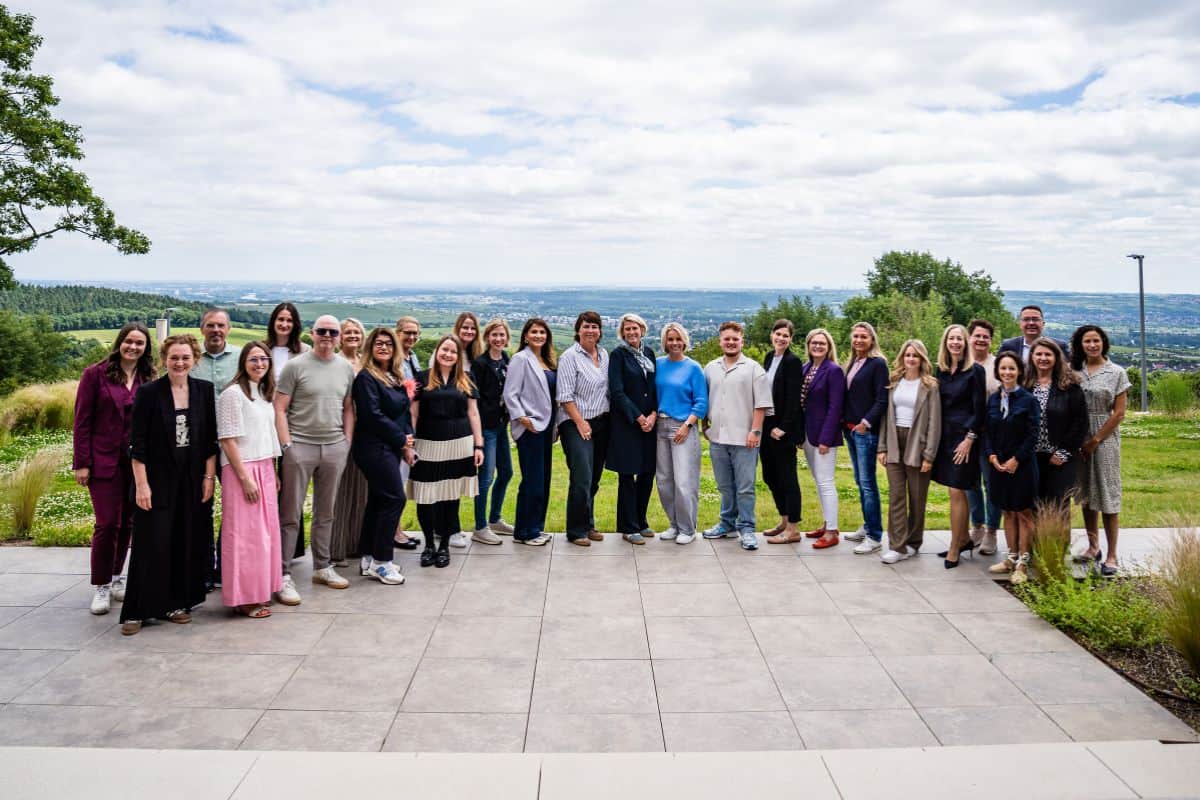 Eine Gruppe von Fachleuten steht auf einer Terrasse mit Blick auf eine grüne Landschaft unter einem bewölkten Himmel.