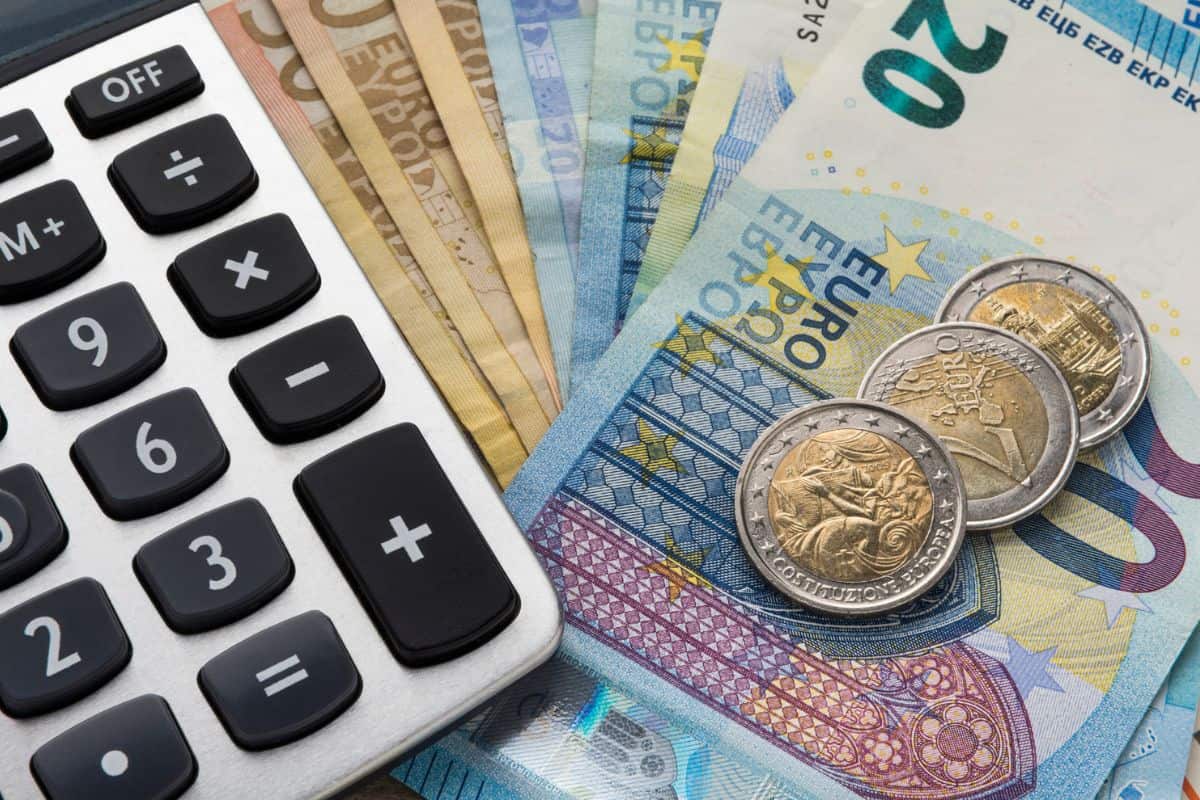 Ein Taschenrechner liegt auf einem Stapel von Euro-Banknoten und Münzen, die verschiedene Werte darstellen.