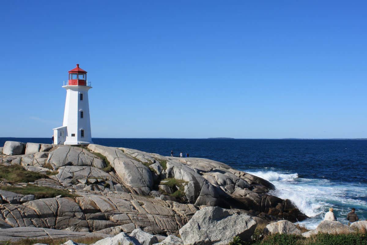 Ein Leuchtturm an der Küste von Nova Scotia, umgeben von felsigen Ufern und dem offenen Ozean unter klarem blauen Himmel.