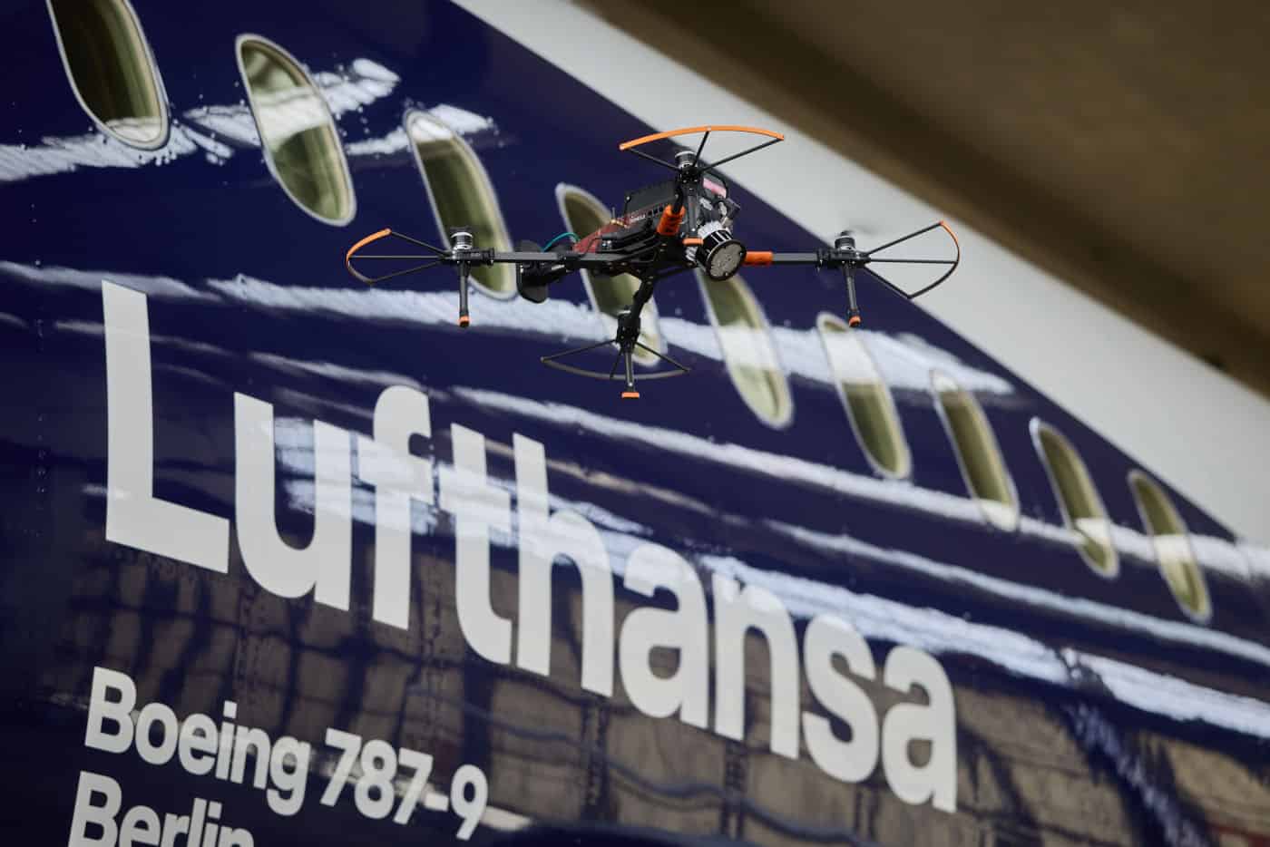 Eine Drohne schwebt vor einem Lufthansa-Flugzeug mit dem Schriftzug und der Modellbezeichnung Boeing 787-9 im Hintergrund.